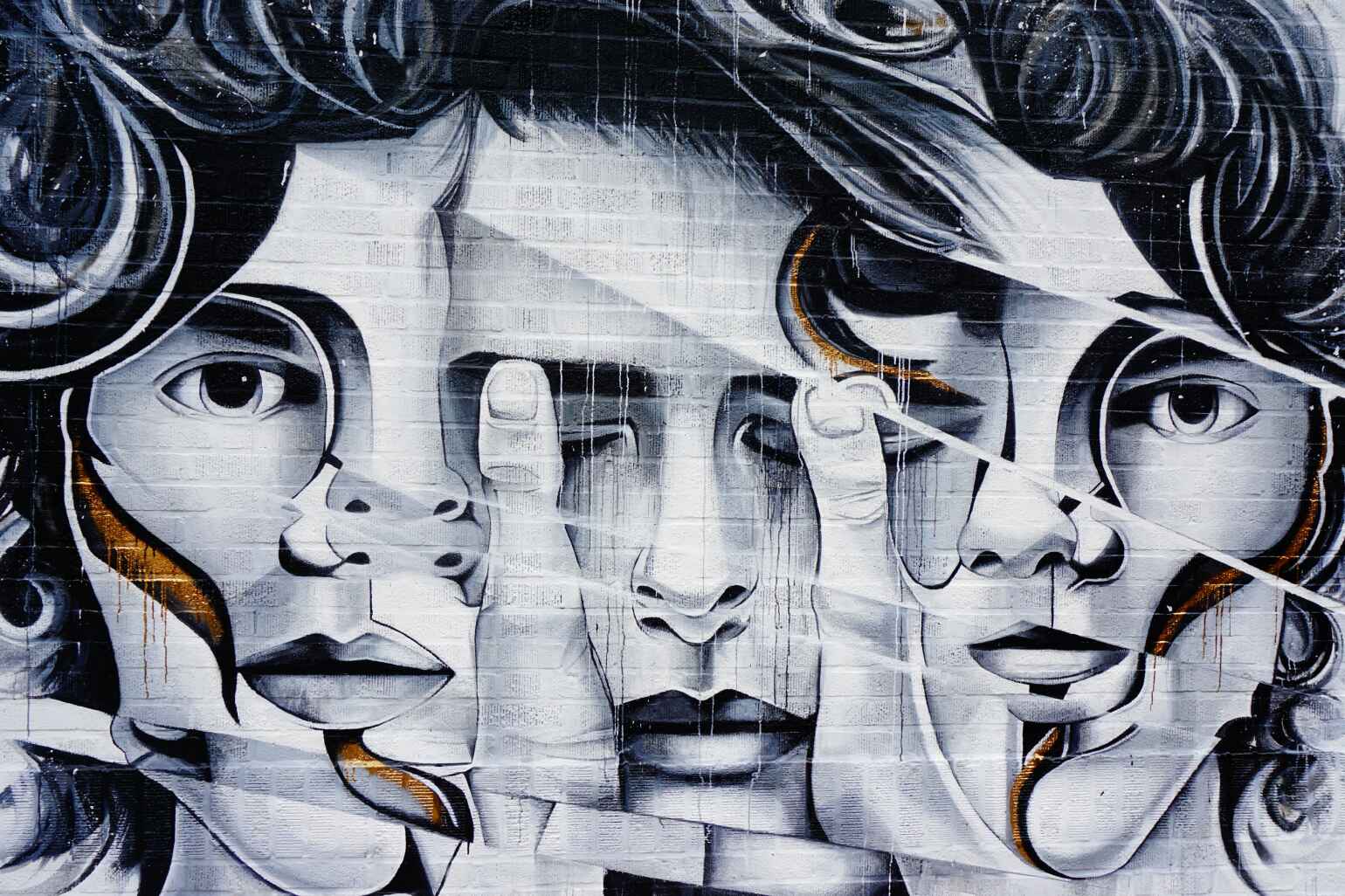 A large mural of three abstract male faces next to one another, with the middle held with thumbs covering the eyelids and jagged lines running diagonally from top left to bottom right